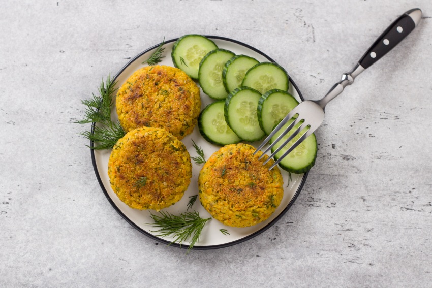 Delicious millet cutlets with carrots and seeds served with cucumber and herbs on a gray textured background, top view. Homemade vegan food